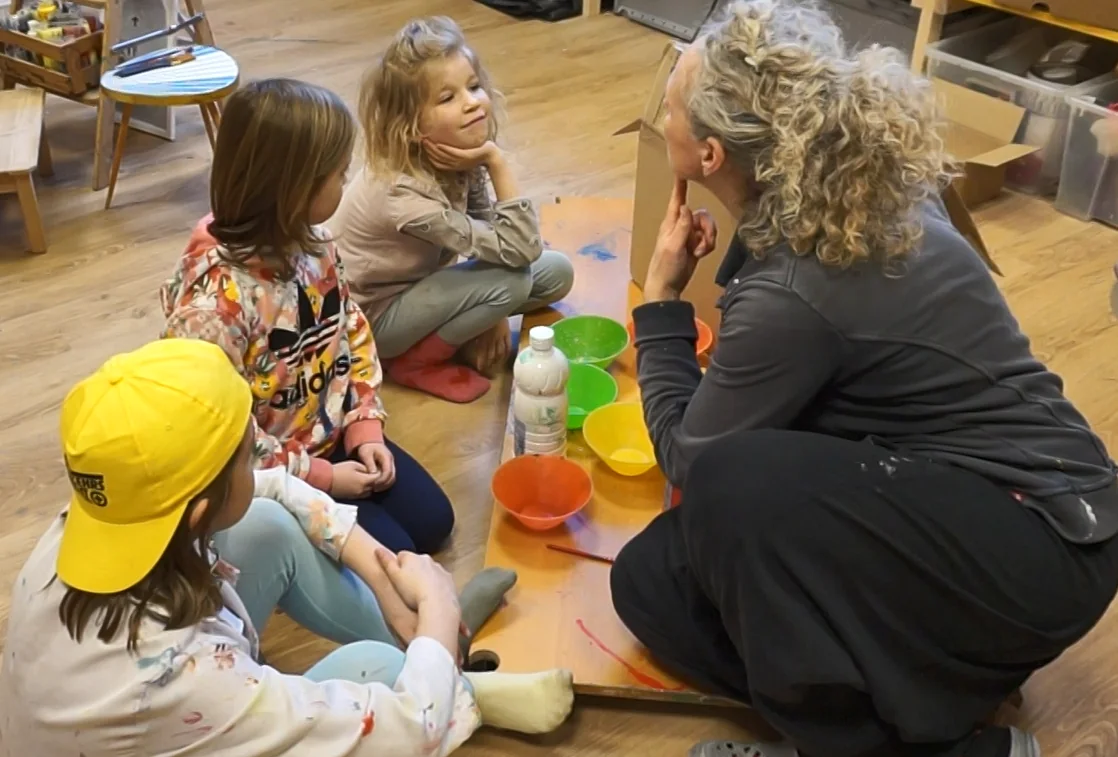 Pädagogische Fachkraft im Gespräch mit einer kleinen Kindergruppe in einer Alltagssituation